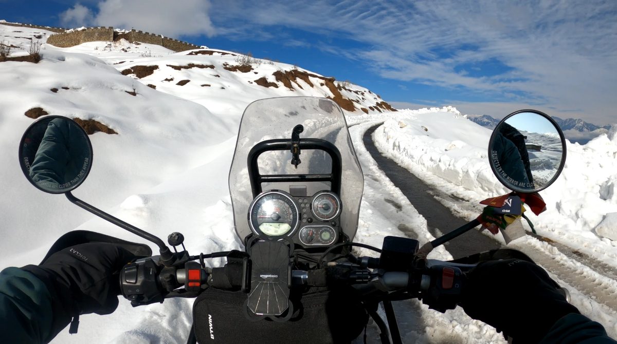 Riding a motorbike up a snowy mountain road, a fort wall on the hill above